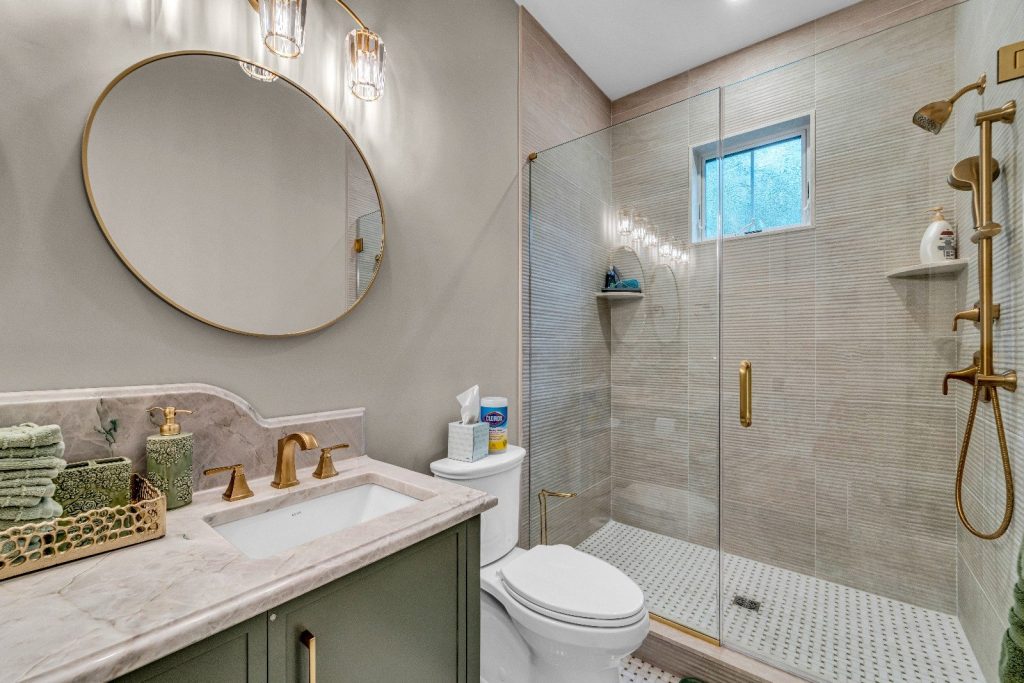 Modern bathroom remodel by Kitch Designs — walk-in shower, brass fixtures and round mirror