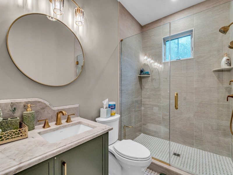 Modern bathroom remodel by Kitch Designs — walk-in shower, brass fixtures and round mirror